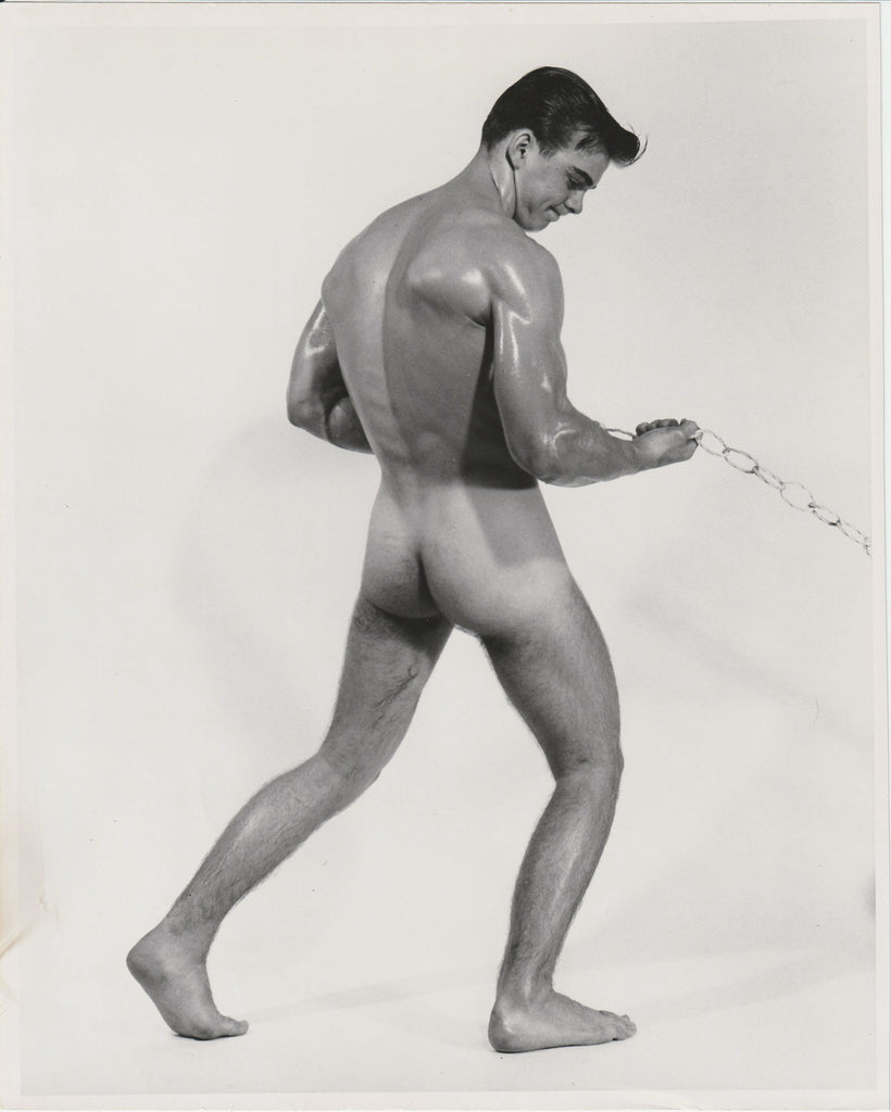 Black and white Bruce of LA gay physique photograph of a muscular nude male model from behind, holding a chain, Jim Conrey.