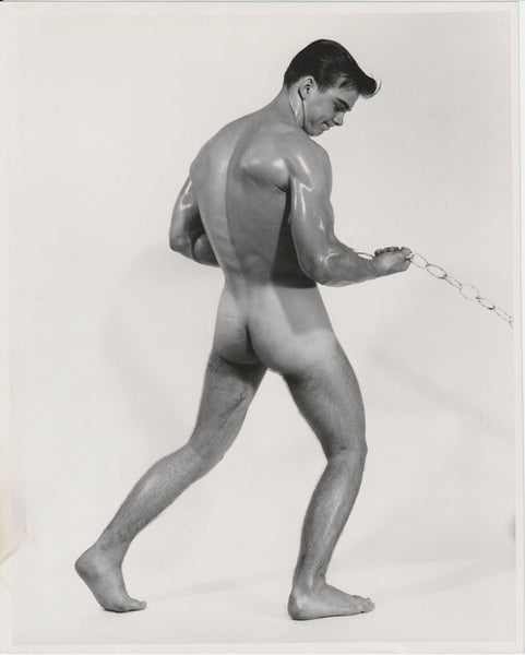 Black and white Bruce of LA gay physique photograph of a muscular nude male model from behind, holding a chain, Jim Conrey.