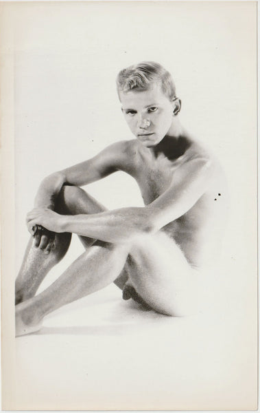 A black and white artistic studio photograph of a seated nude male figure.