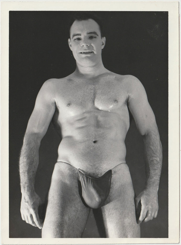 A black and white physique photograph of male model wearing a dark posing strap, Art Ullrich.