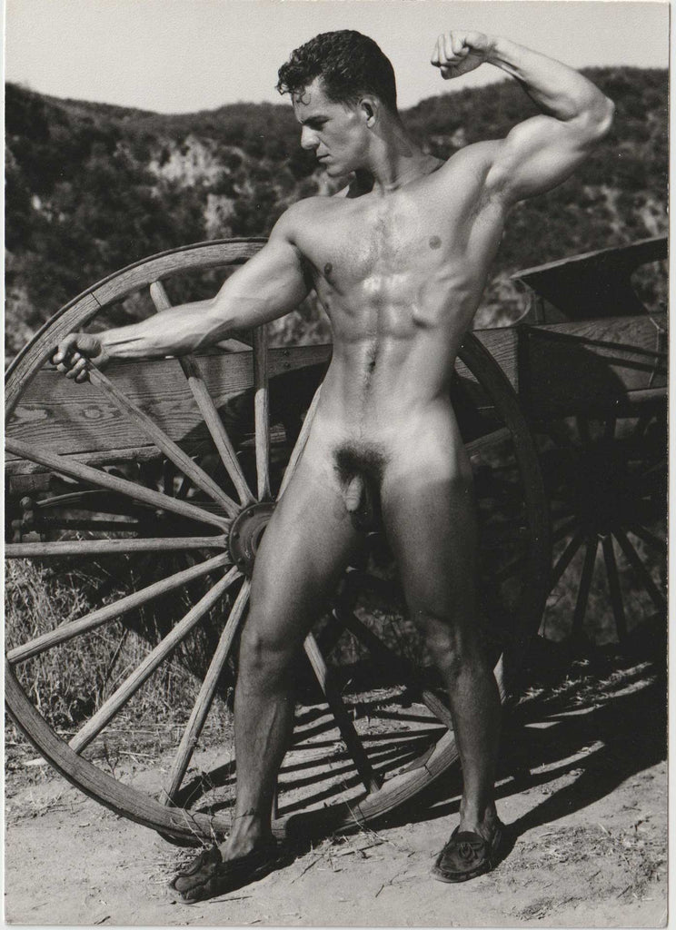 Vintage photo of handsome muscular Dick Spero flexing next to a wagon