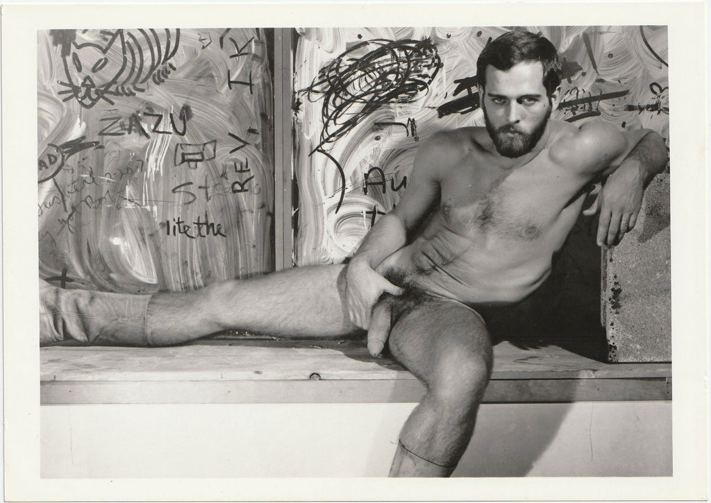 Naked man sitting on a wooden bench with graffiti in the background. Vintage Target Studios photo.