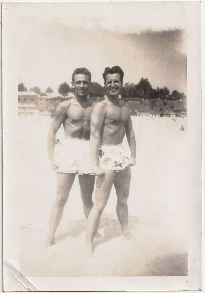 Two handsome guys smile and flex on the beach. Vintage gay snapshot