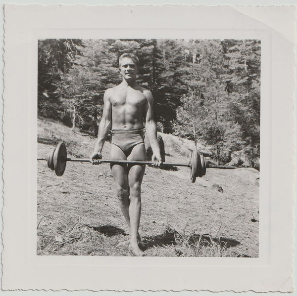 Man lifting a barbell outdoors with trees in the background vintage gay photo