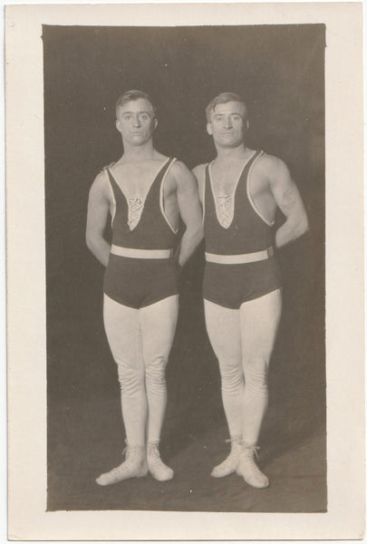 Pair of acrobats pose with hands behind back, feet turned out, and very serious expressions. 4" x 6" vintage photo