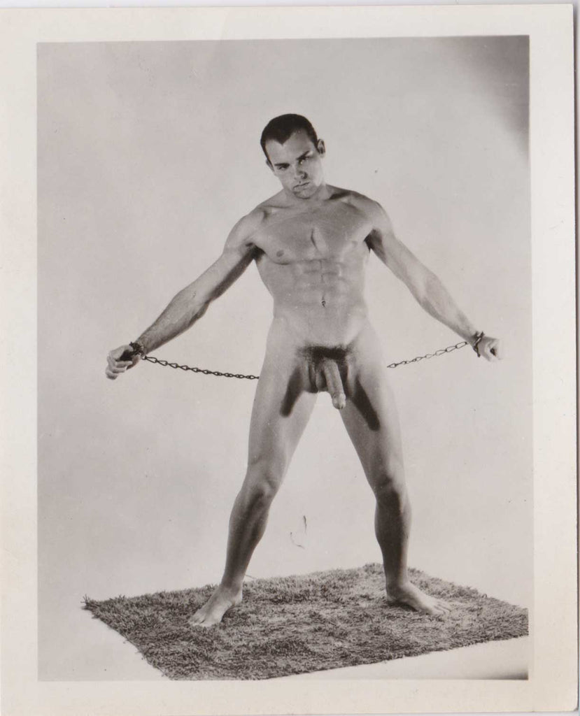 Vintage male nude Handsome guy with "Eddie Munster" hair style sands on a shag rug, his wrists chained.