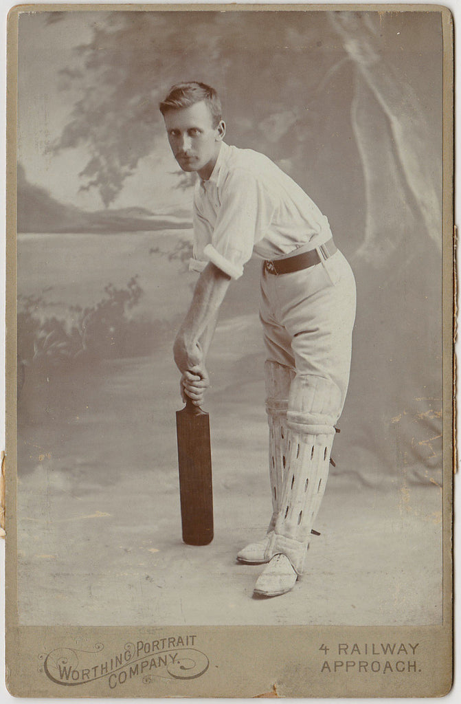 Vintage photograph of a handsome man holding a cricket bat  in a studio setting.