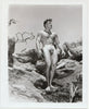 Handsome hunk Dave Lancaster stands naked on a rocky hillside.