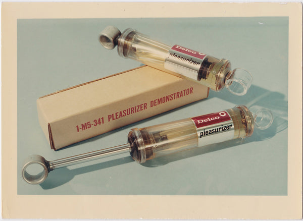 Two 'pleasurizer' devices with a box labeled 'Delco' on a light blue background.
