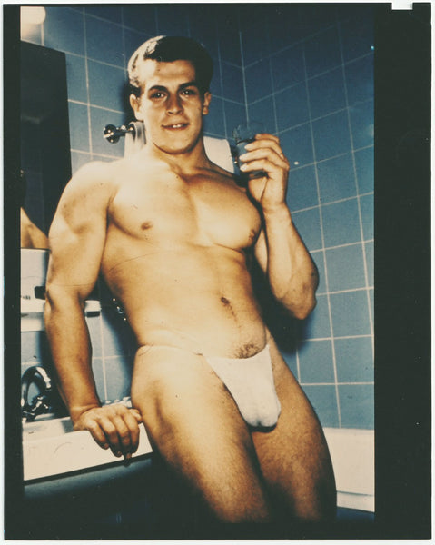 Handsome muscular young Helmut Reidmeier poses in the bathroom holding a glass. Vintage gay photo.