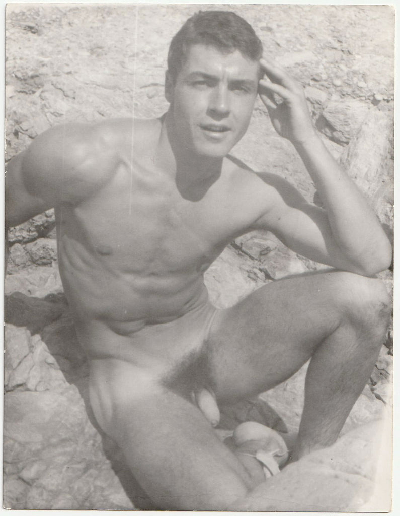 Handsome Jean Pierre Martin sitting on some rocks, squinting in the sunshine. Gay physique photo attributed to Barrington.