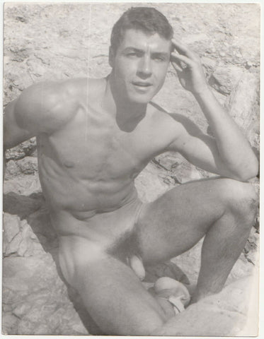 Handsome Jean Pierre Martin sitting on some rocks, squinting in the sunshine. Gay physique photo attributed to Barrington.