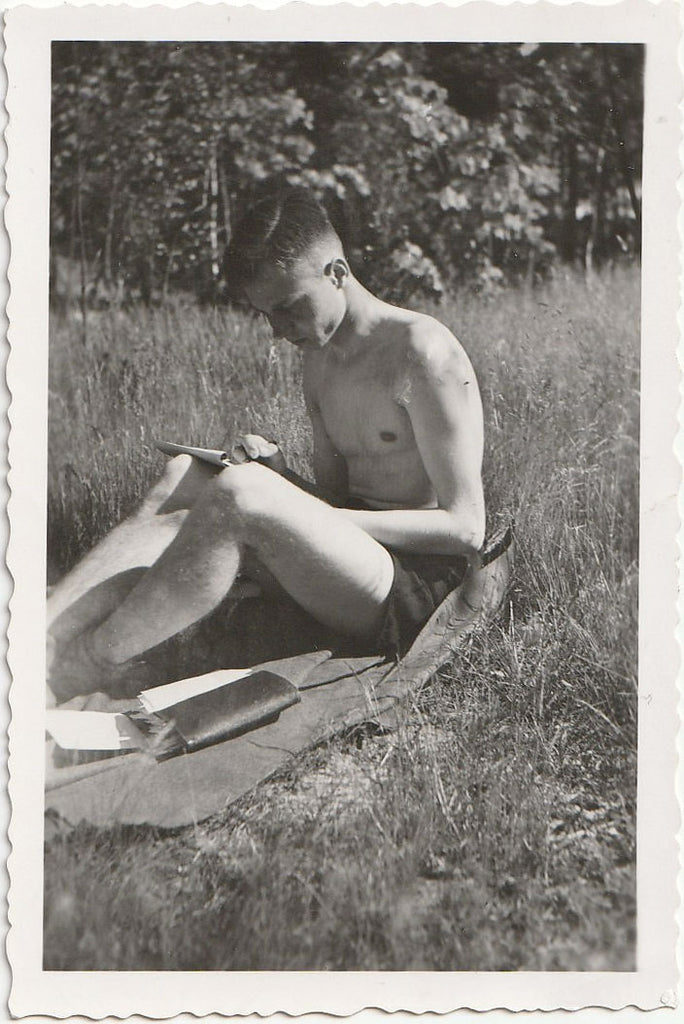 Handsome young man sitting on a blanket in the sunshine, appears to be writing in a journal.
