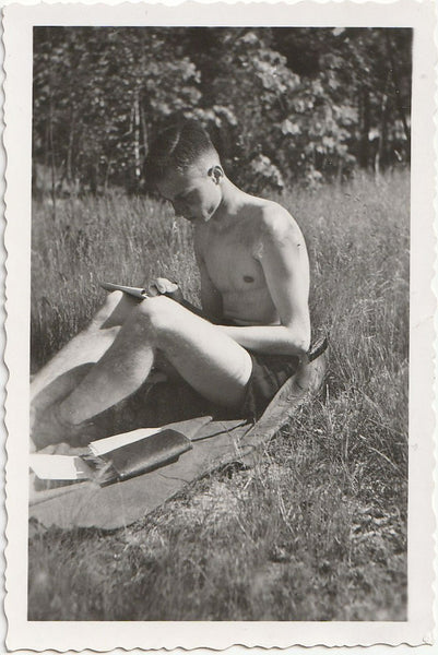 Handsome young man sitting on a blanket in the sunshine, appears to be writing in a journal.
