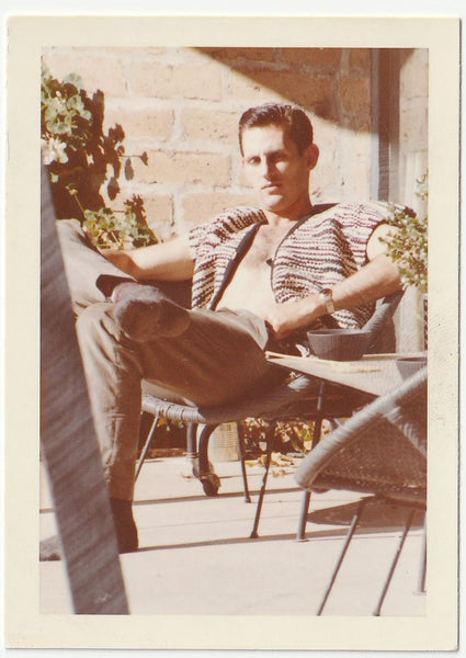 A vintage-style photograph showing a man reclining in a patio chair, wearing a patterned knit vest, gay interest.