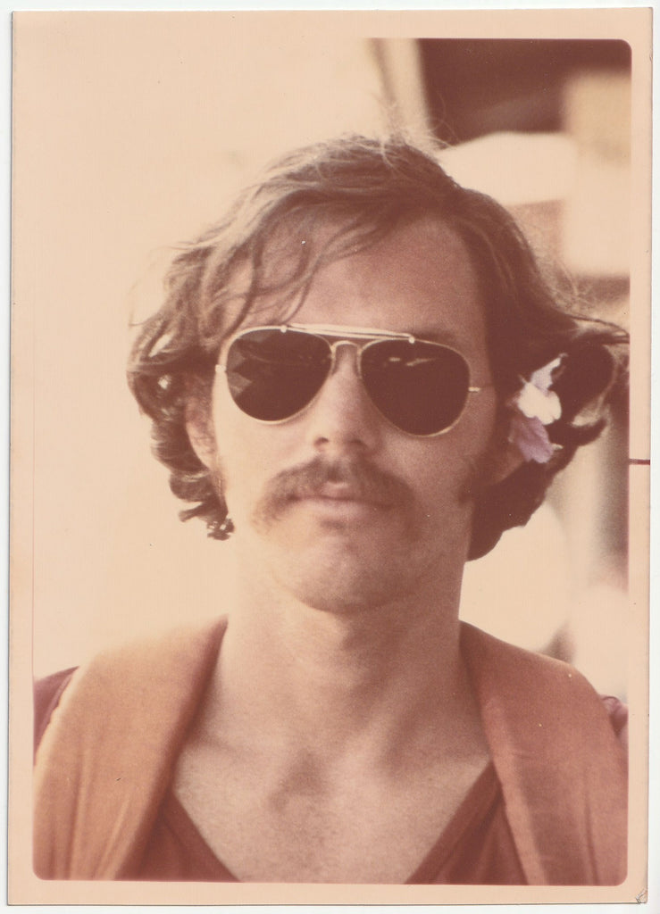 Vintage photo of a man wearing aviator sunglasses with a flower in his hair.