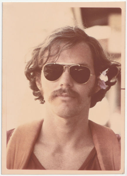Vintage photo of a man wearing aviator sunglasses with a flower in his hair.