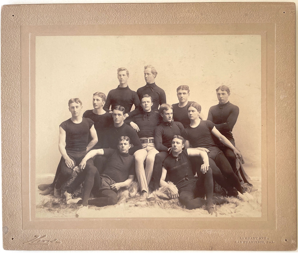 Large format photo of 12 members of an unidentified team relaxing on (wolfskin?) rugs, San Francisco, 1890s.
