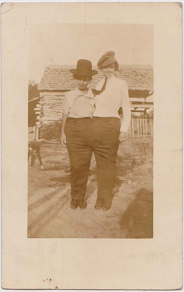 Vintage sepia Real Photo Postcard of two young women crammed into a pair of man's pant