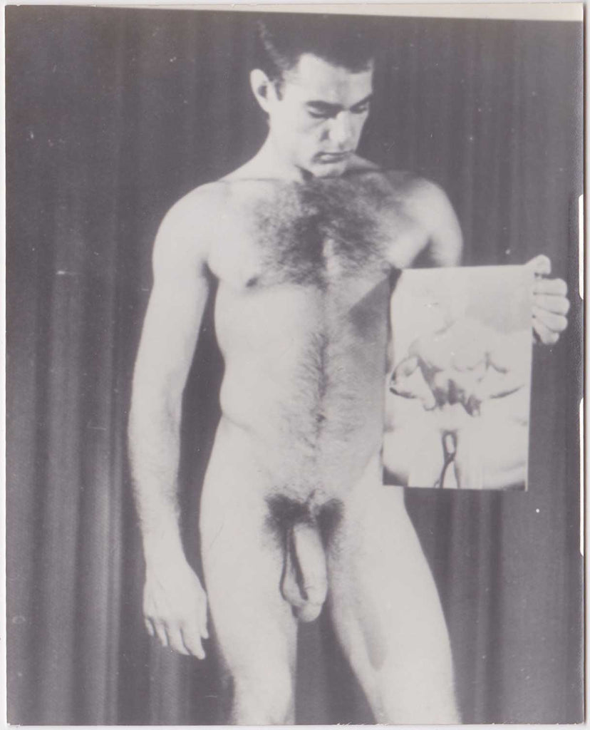 unusual image of a standing, hair-chested male nude holding a large photo of a male nude bodybuilder. 