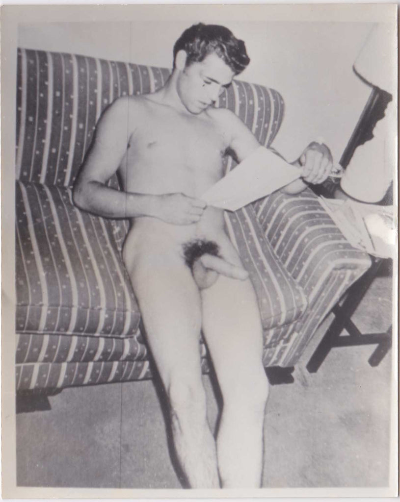 Handsome dark-haired male nude on sofa, reading what must have been a very stimulating page.