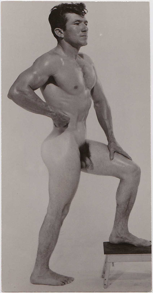 Vintage photo of a male nude with one foot on a small stool and one hand at his waist.