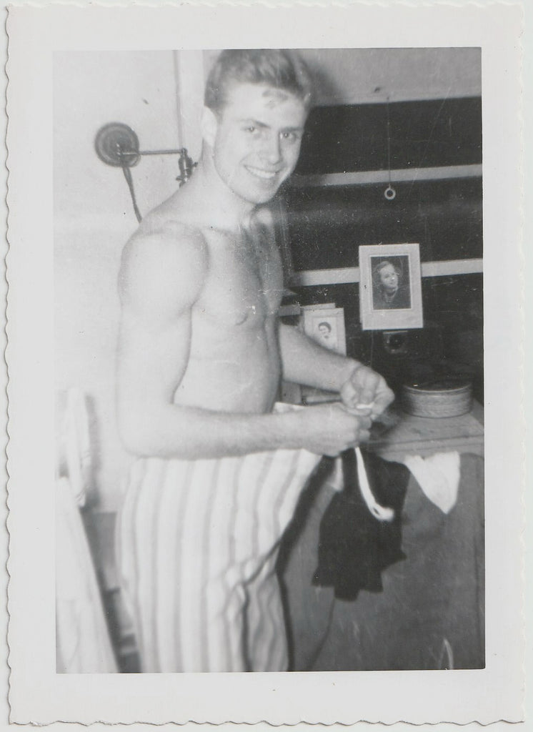 vintage black and white photograph of a young man standing shirtless tying the strings of his pajama bottoms.