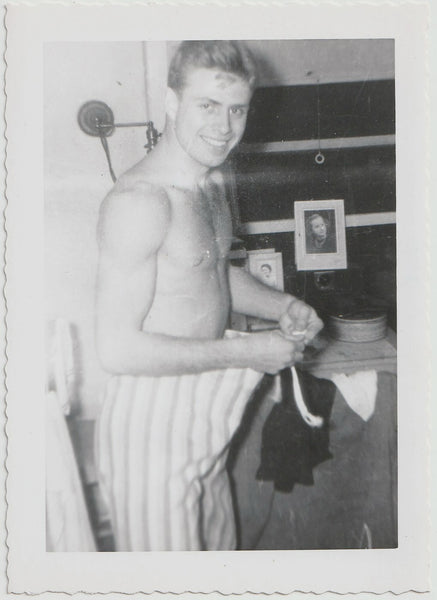 vintage black and white photograph of a young man standing shirtless tying the strings of his pajama bottoms.