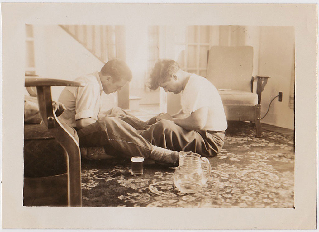 They sit on a carpeted floor with a full glass and an empty beer pitcher, intently focused on some task Vintage Sepia Snapshot