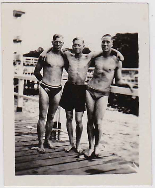 Three affectionate men stand on a wooden pier in their swimsuits. vintage gay snapshot photo
