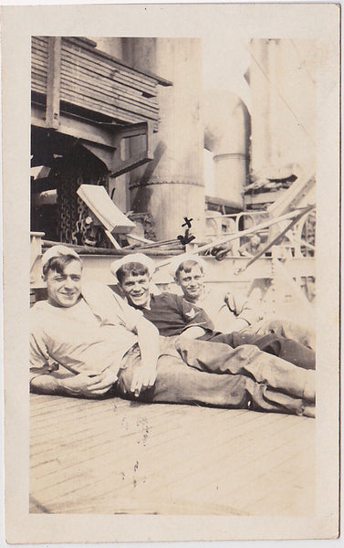 3 smiling sailors recline on deck