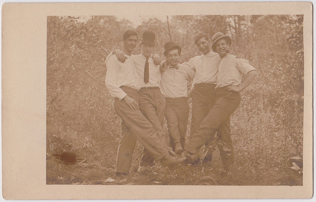Vintage sepia Real Photo Postcard of five affectionate men sticking out one leg to join their feet in the middle.