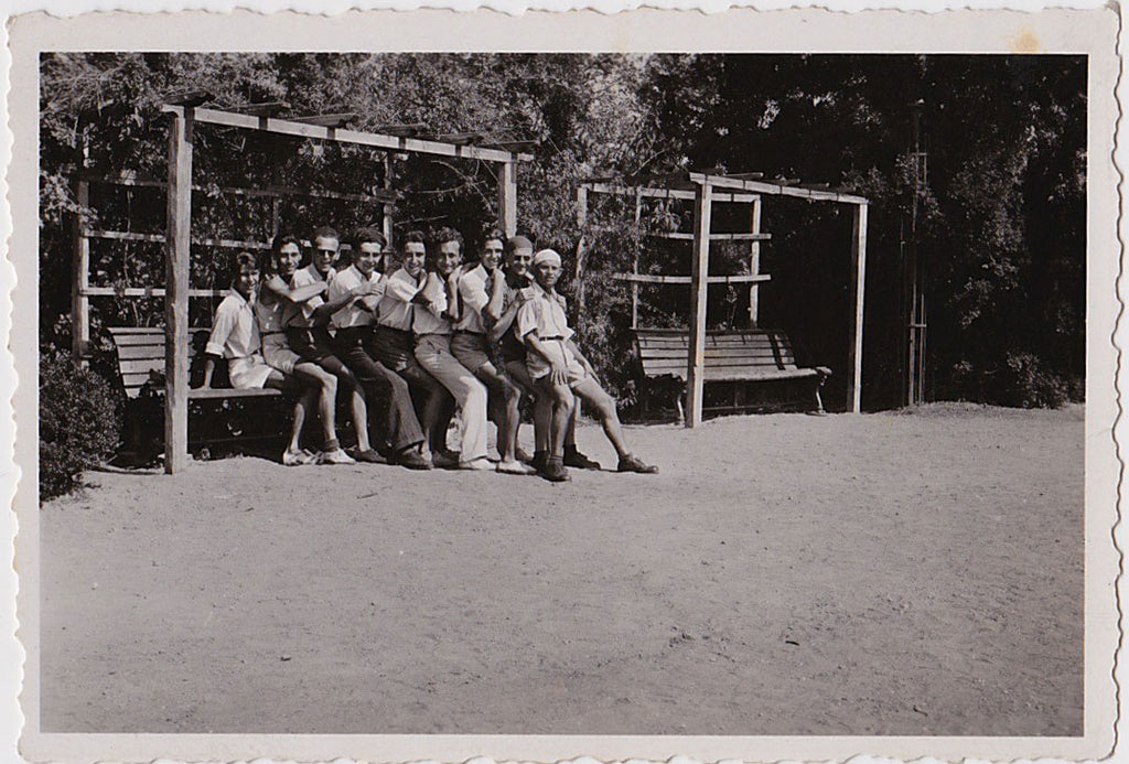 One man sitting on a bench with eight men on his lap, vintage snapshot 1950.