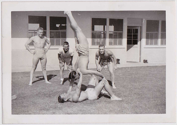 Two hand balancers are closely watched by three studly buddies. Vintage black and white photo