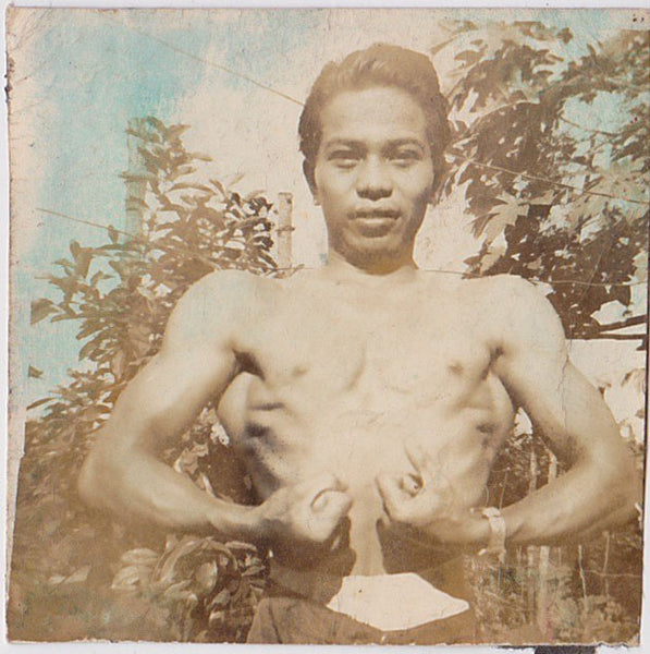 Undated hand-tinted vintage sepia photo of an Asian man flexing outdoors. 