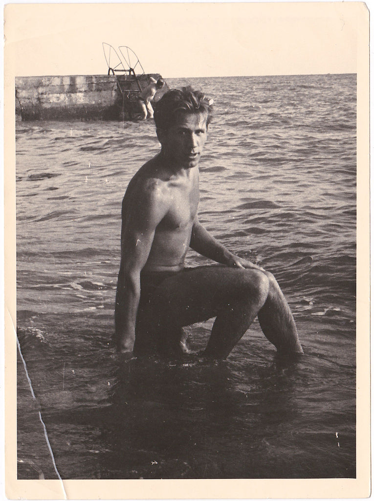 Handsome guy sits on a rock with his feet in the water. Vintage photo gloss finish, dated 1960.