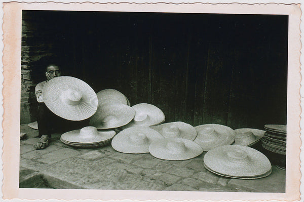 Beautifully composed image of a hat vendor almost hidden behind his large straw hats. 