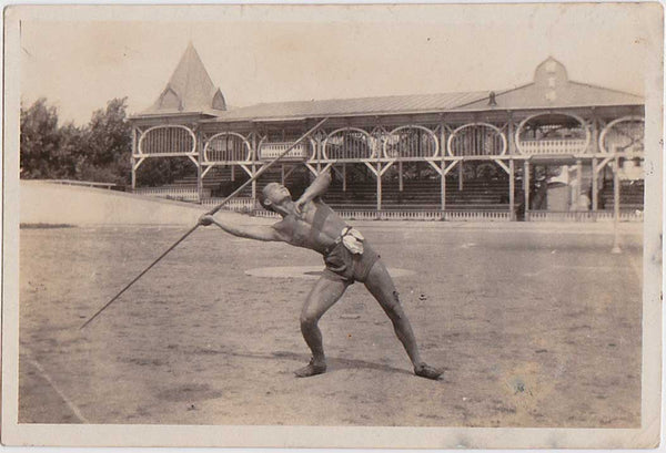 Vintage snapshot Muscular athlete about to let his javelin fly. Interesting structure in background.