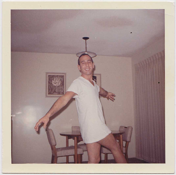 Vintage color snapshot of a guy dancing alone in his dining room wearing only a long t-shirt. 