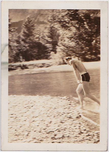 Strange little snapshot of a guy in a swimsuit loping along the edge of a river