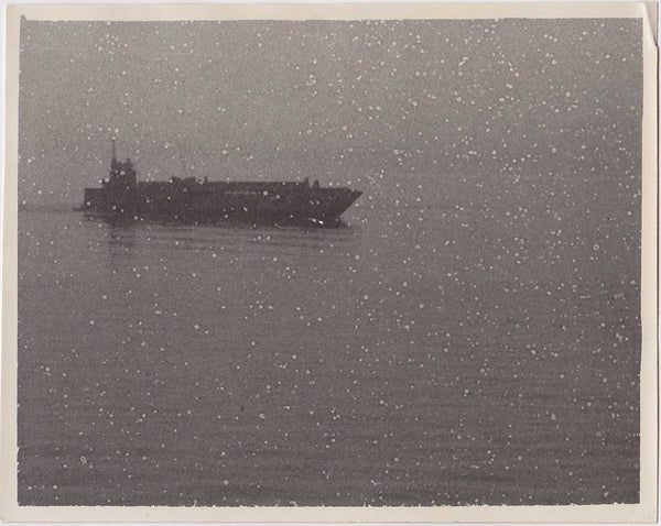 Peaceful image of a warship seeming to glide across the ocean during a snowstorm.
