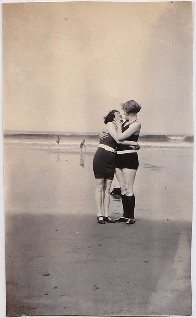 Two affectionate women share a romantic moment together on the beach, gazing into each others' eyes, vintage photo